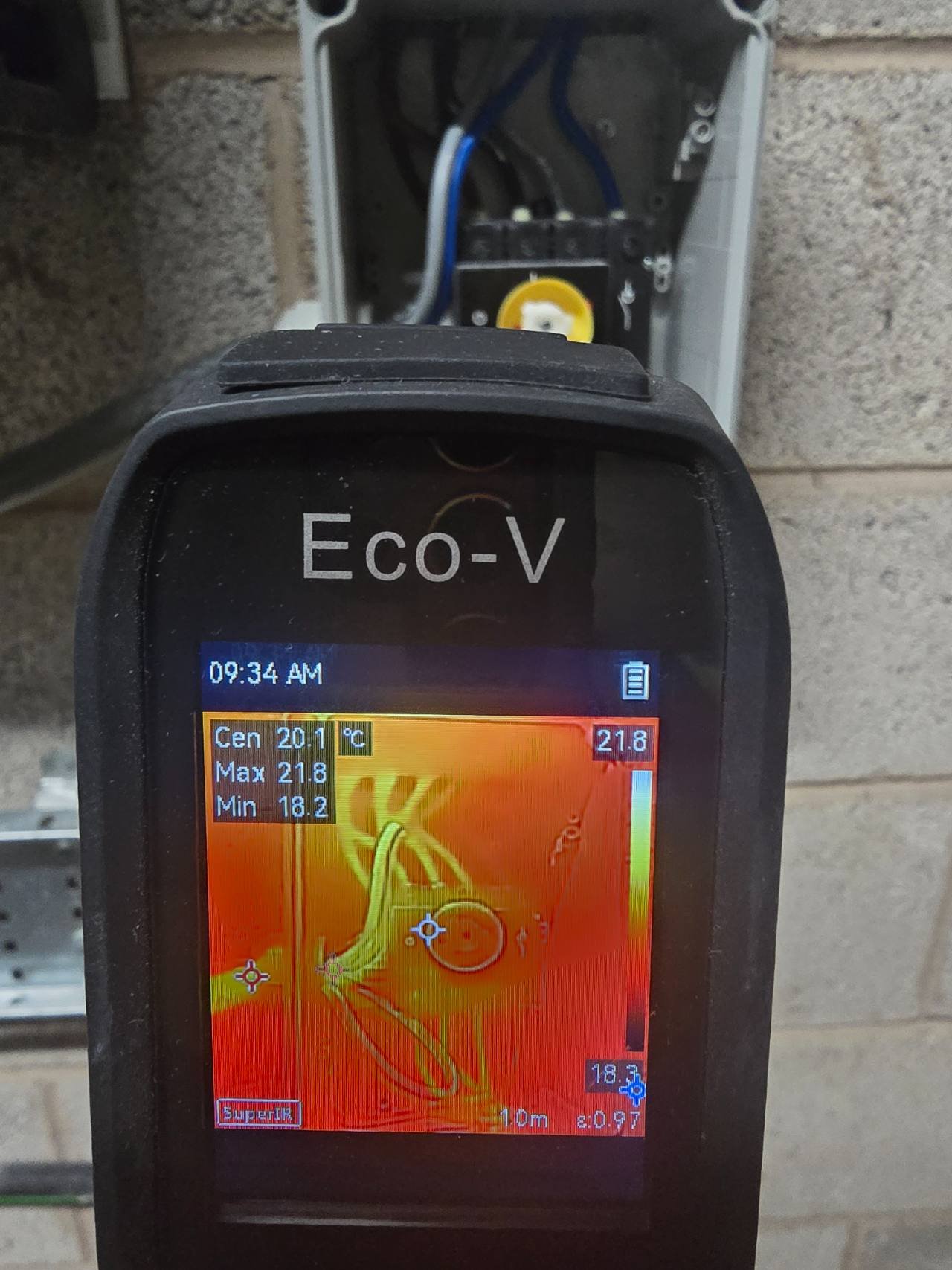 Handheld thermal camera inspecting an open isolator enclosure during a service visit