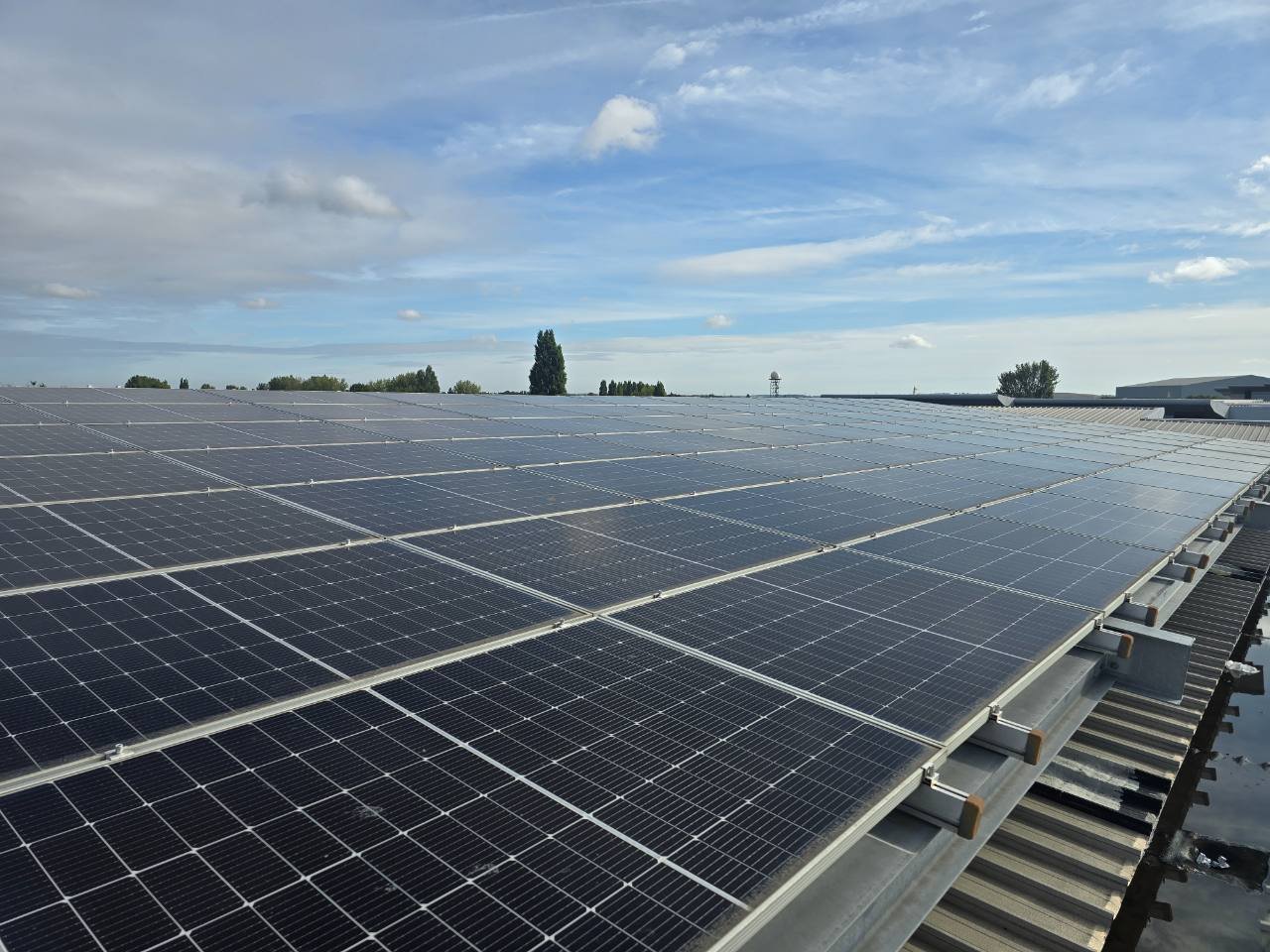 Large commercial solar array across a metal industrial roof under blue sky
